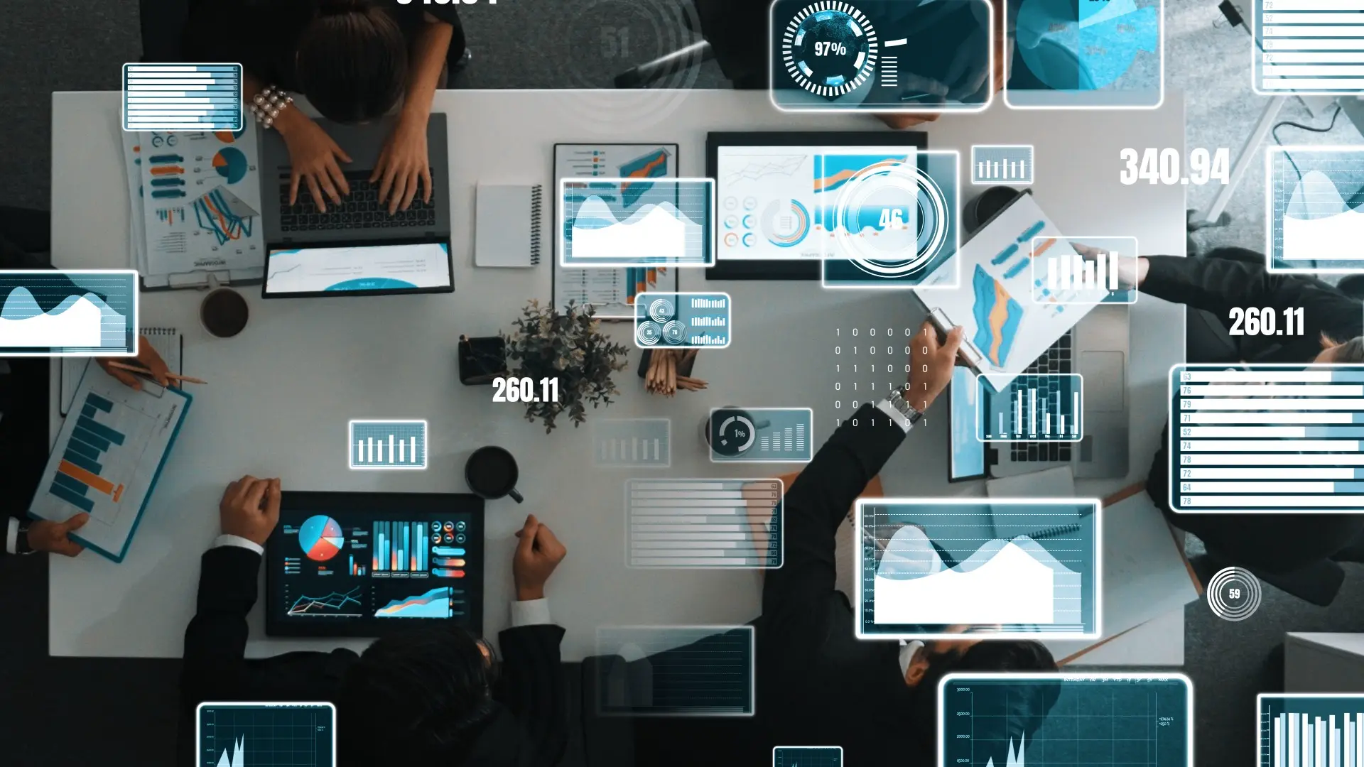 Top-down view of business people discussing financial strategy with documents, tablets, and analytics dashboards on a meeting table